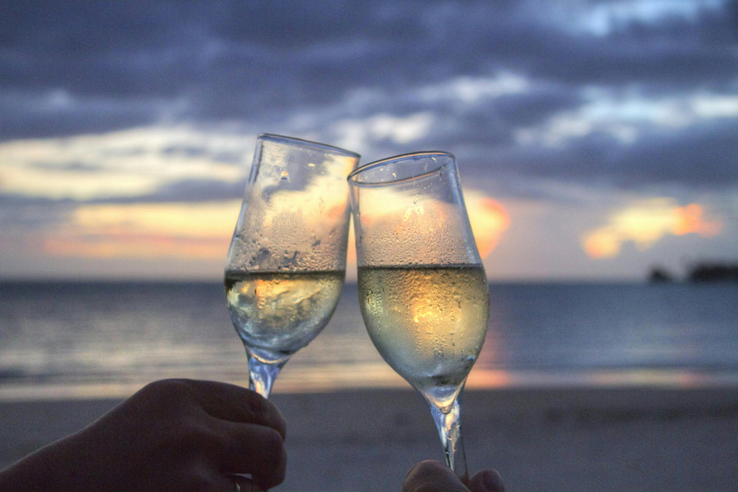 Twee glazen witte wijn klinken tegen elkaar bij zonsondergang, een perfecte avond met elegantie en smaak.