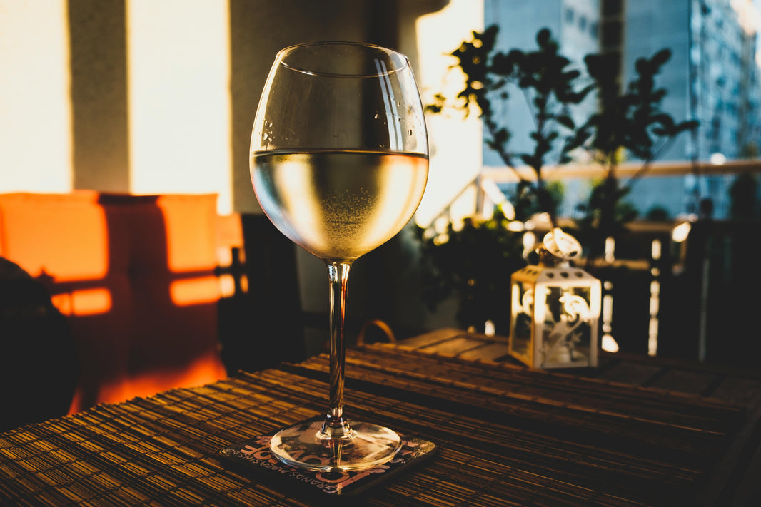 Een hand houdt een glas witte wijn vast bij een gedekte tafel.