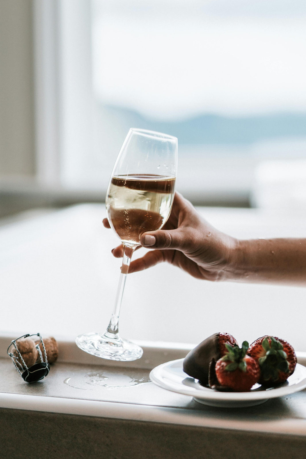 Glas witte wijn met chocolade-aardbeien op een wit bord in een elegante setting.